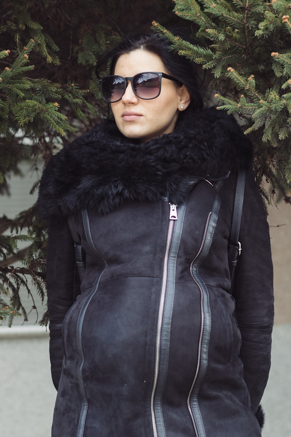 Добре изглеждаща млада жена, носеща слънчеви очила и кожено кожено палто