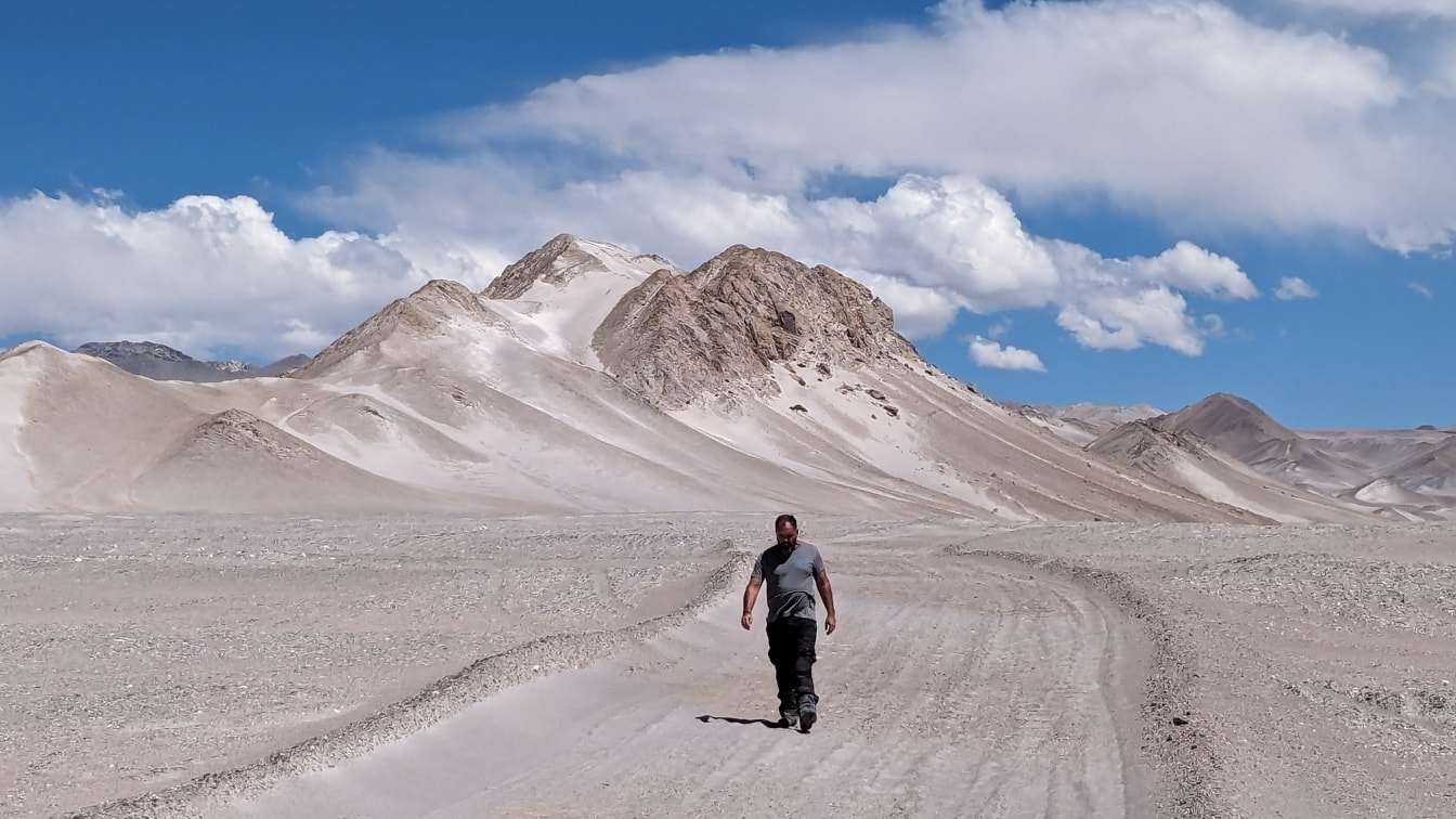 ผู้ชายคนเดียวในทะเลทรายเดินบนถนนที่เต็มไปด้วยฝุ่นของทะเลทราย Atacama ที่แห้งแล้งมาก