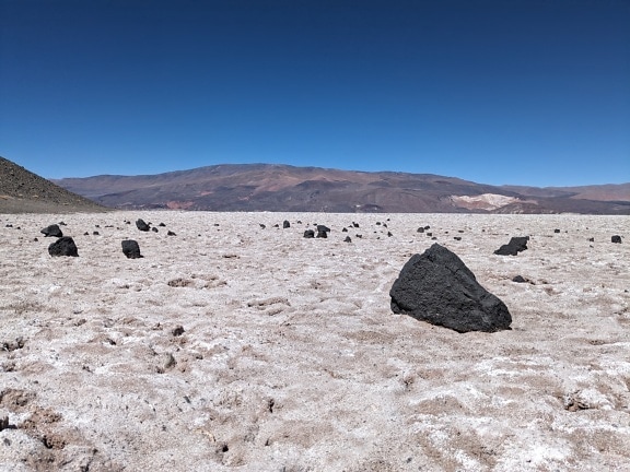 Rocky landscape with black volcanic rocks on the sedimentary deposits of white salt in the desert