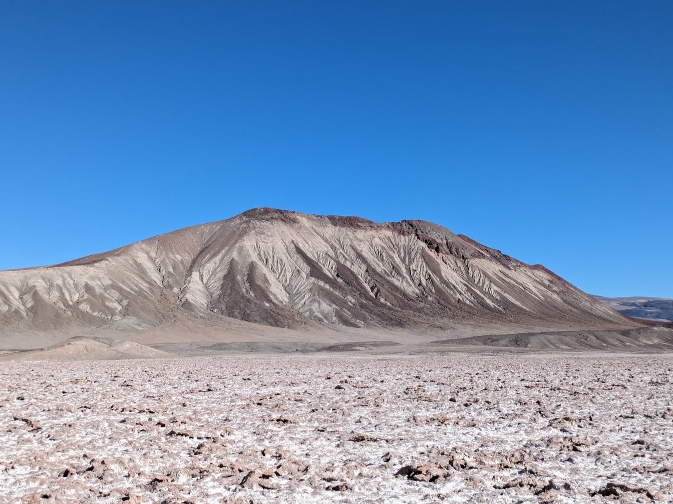 Núi xám trên sa mạc với một bãi muối phía trước nó ở Argentina