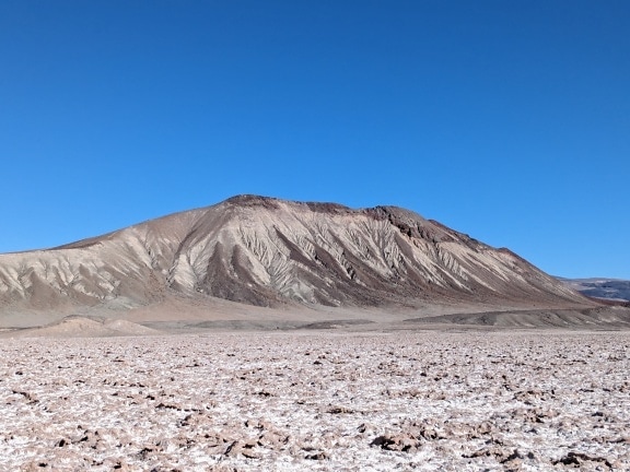 Grey mountain in the desert with a saltflat in front of it in Argentina