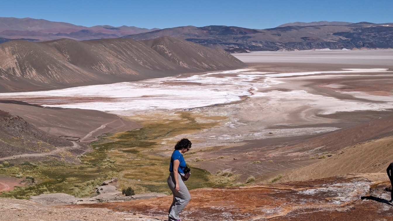 Wanita hiking di puncak bukit gurun dengan dataran tinggi garam di latar belakang