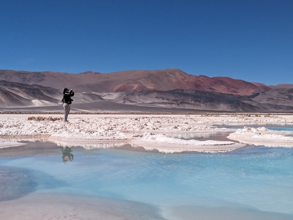 Tourist standing on a beach of desert’s salt lake and photographing landscape of the desert oasis