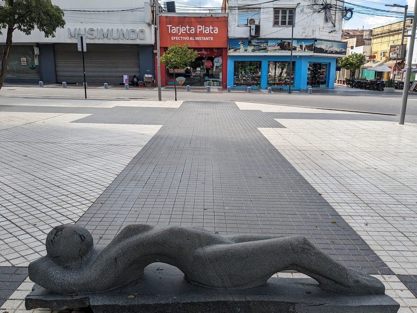 Zwart granietstandbeeld van een vrouw die op een trottoir ligt