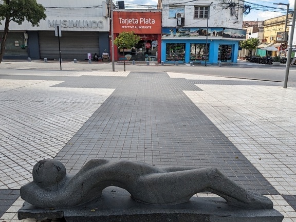 Black granite statue of a woman lying on a sidewalk