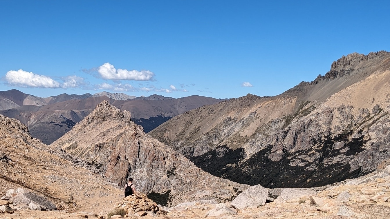 Egy hegymászó ül egy sziklán, és lélegzetelállító panorámát élvez a hegycsúcsokkal körülvett völgyre