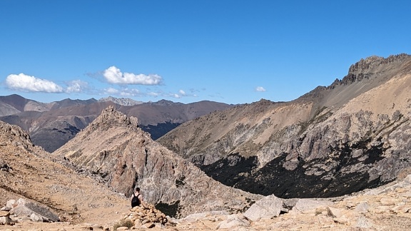 Алпинист, седнал на скала и наслаждаващ се на спираща дъха панорамна гледка към долината, заобиколена от планински върхове