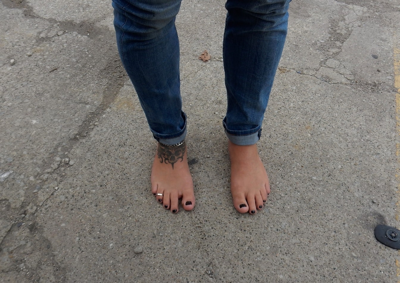 Bosý muž v tmavě modrých džínách s černým lakem na nehty na nohou
