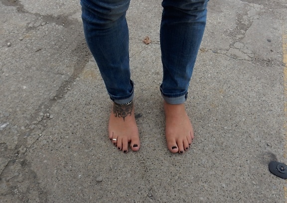 A barefoot man in dark blue jeans wearing black nail polish on his toes
