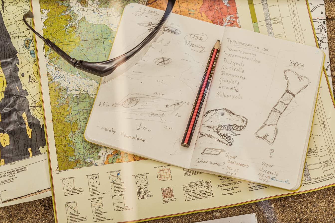 Notatnik z rysunkiem głowy dinozaura i mapą pod nim, przedstawiającą paleontologiczne badania naukowe
