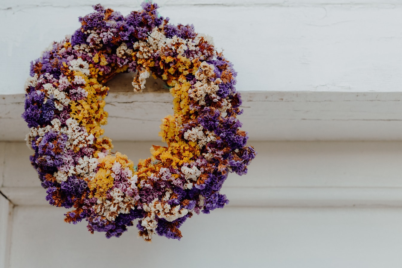 Corona de flores violáceas secas que cuelgan en una pared blanca sobre la puerta principal