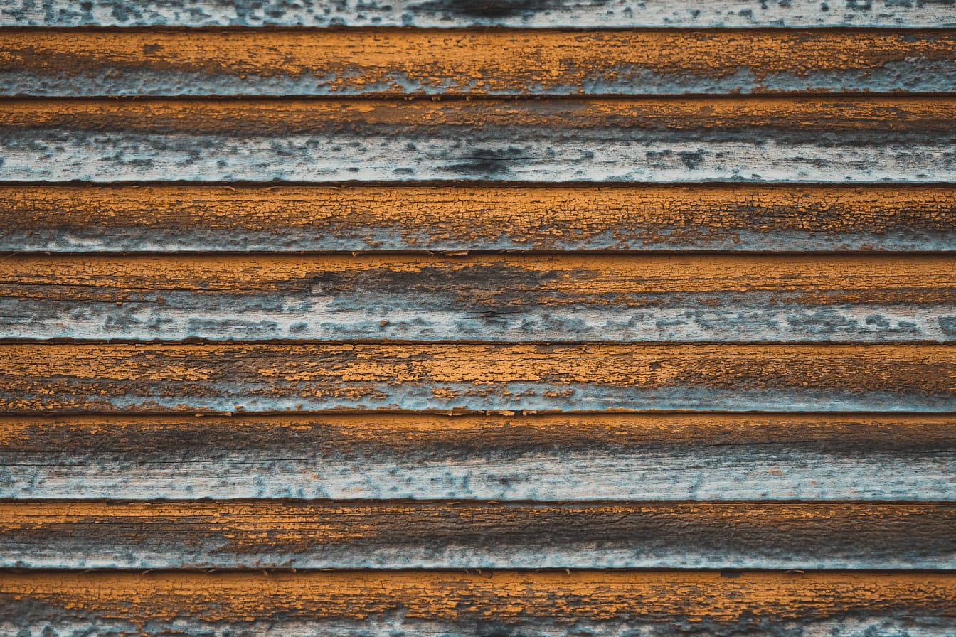 Vecchie tende in legno impilate orizzontalmente dipinte con vernice bruno-giallastra che si stacca