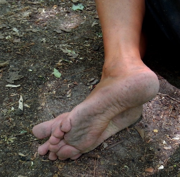더러운 땅을 밟고 있는 맨발의 남자 발 클로즈업
