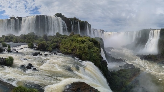A misty landscape of the Iguazu waterfall with green plants and rocks on cliffs