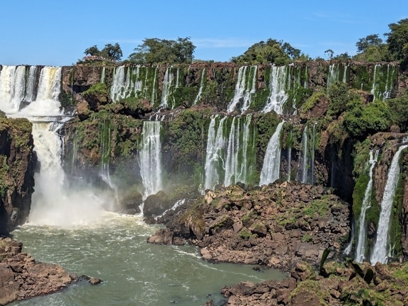 ภูมิทัศน์อันงดงามของแม่น้ํา Iguazu ที่มีน้ําตกและต้นไม้สีเขียวบนหน้าผา