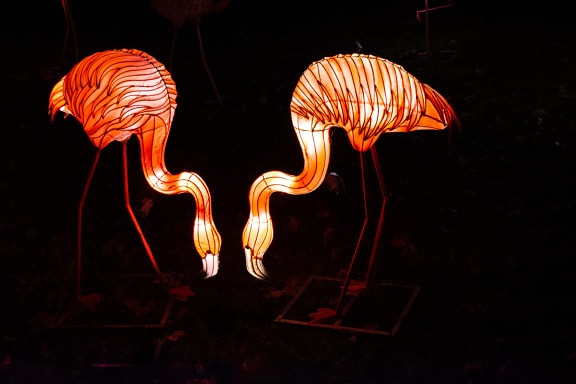 Flamingo sculptures illuminated at night in complete darkness