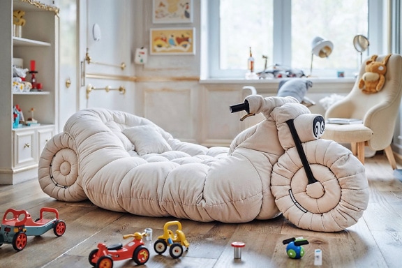 Matratze zum Spielen in Form eines Dreirads auf dem Boden des Kinderzimmers mit Spielzeug drumherum
