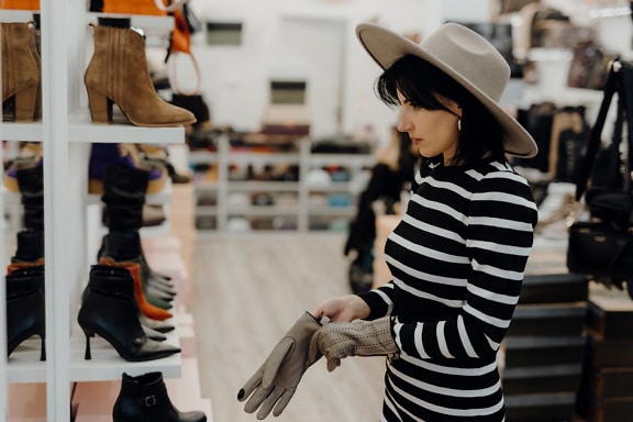 Žena si vyskúša klobúk a rukavice v obchode s oblečením a obuvou