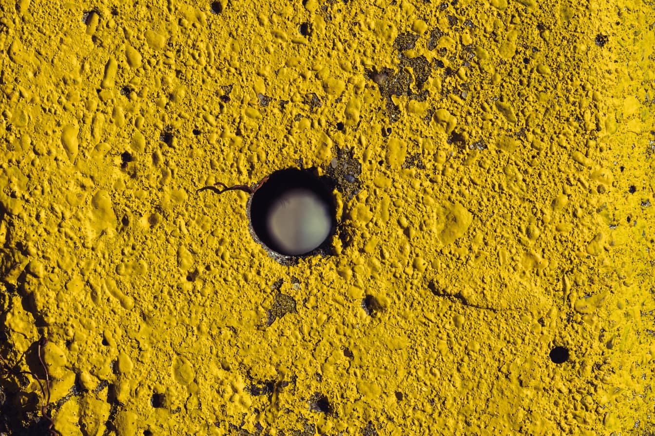 La textura de la superficie de hormigón grueso pintado de amarillo con un pequeño agujero