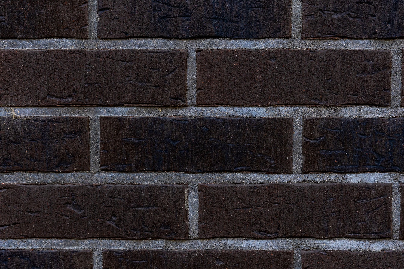 Textur av horisontellt staplad mörkbrun rustik tegelsten med vit cement