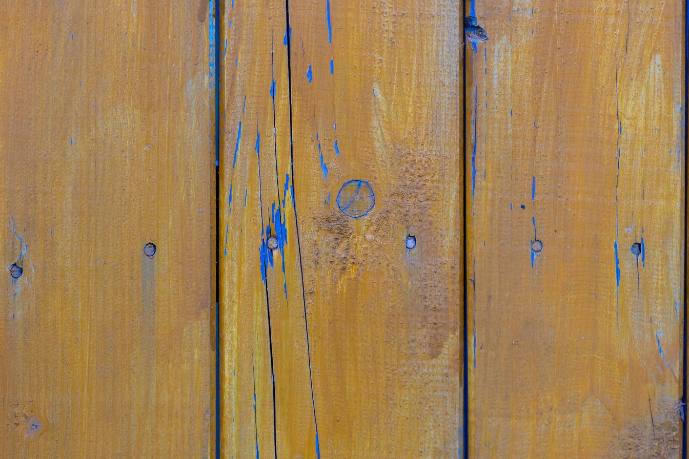 Close-up van verticaal gestapelde houten planken die geelachtig bruin worden geschilderd waaronder blauw is