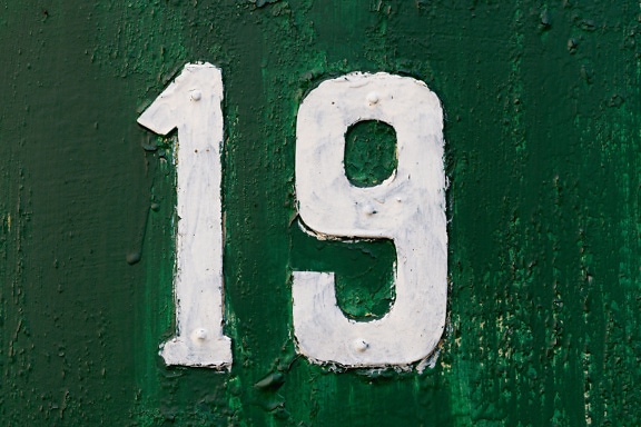 Metal number 19 painted with white paint on dark green metal surface