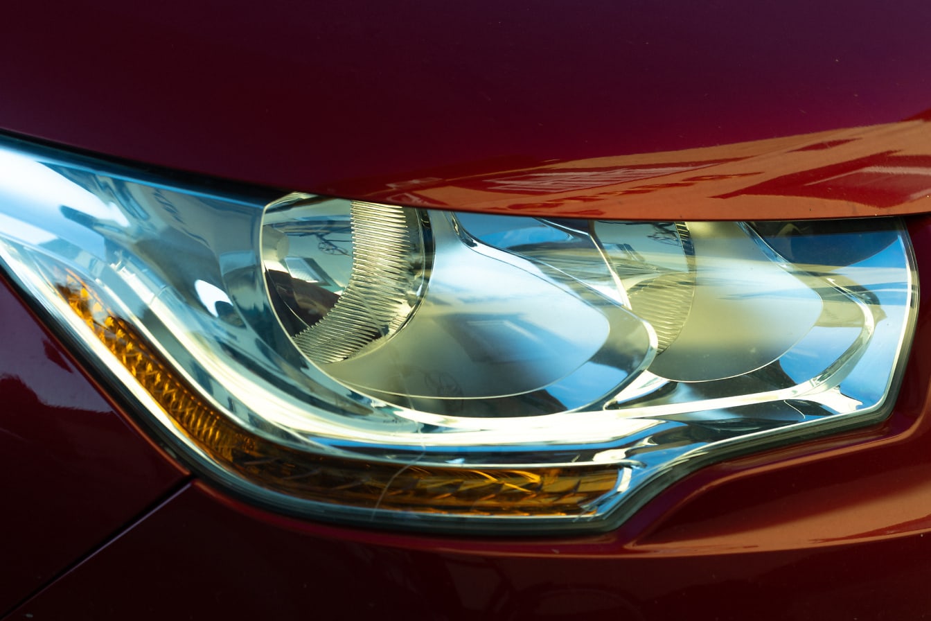 Nærbilde av en frontlykt av en bil med metallisk mørkerød lakk