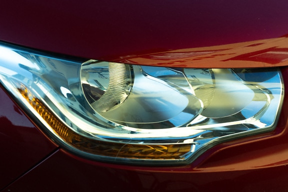 Close-up of a headlight of a car with metallic dark red paint