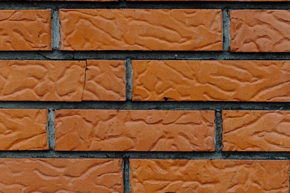 Ziegelwandstruktur mit horizontal gestapelten rötlichen Fassadenziegeln und dunklem Zement