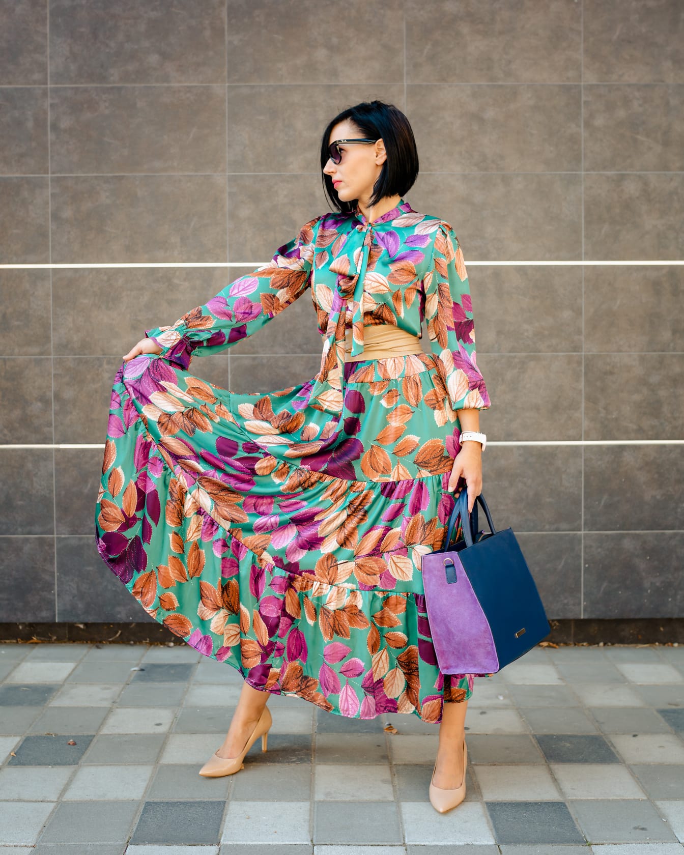 Štíhla mladá dáma pózuje vo farebných šatách a fialovej módnej kabelke
