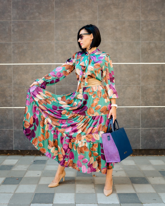 Стройная барышня позирует в красочном платье и фиолетовой модной сумочке