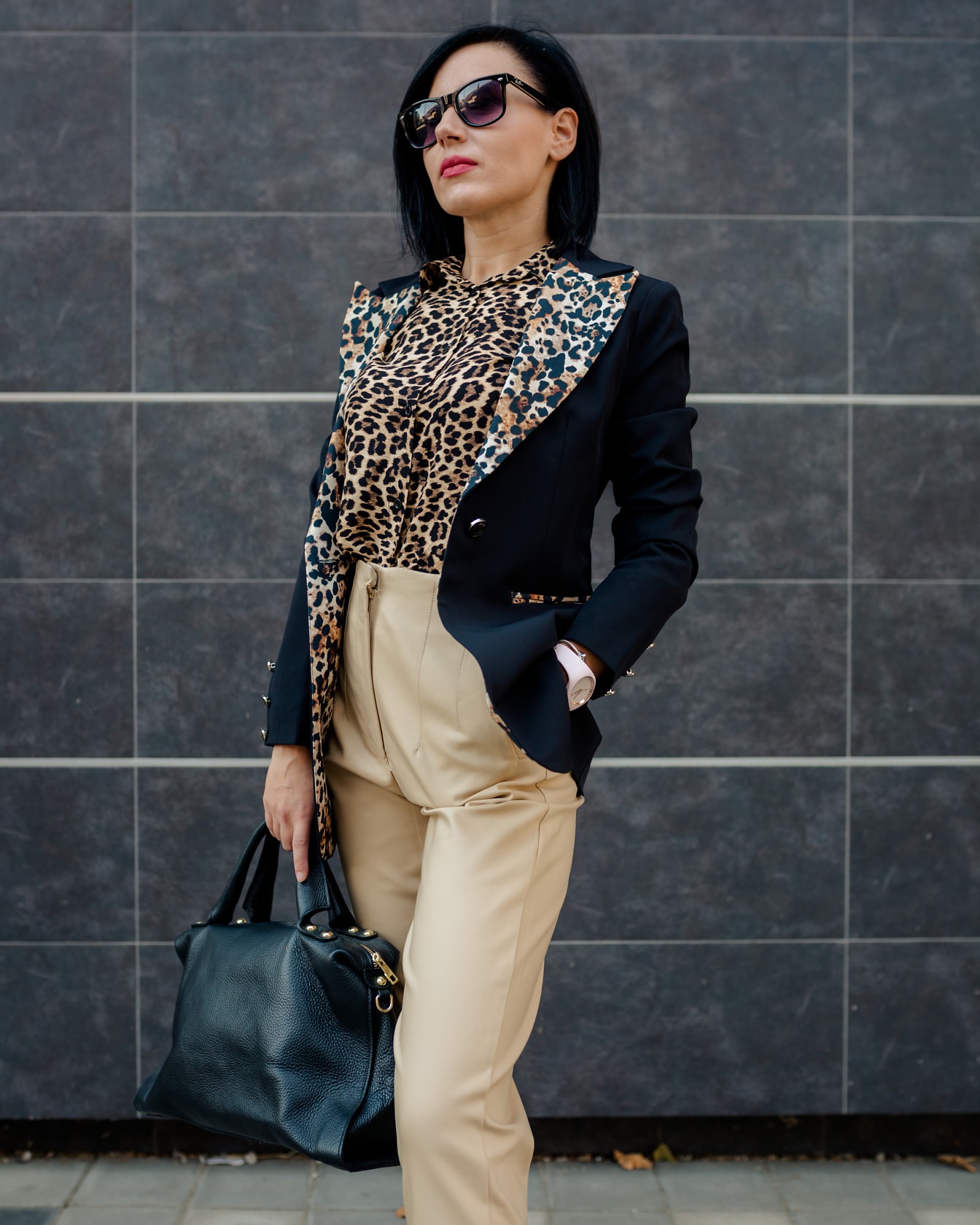 Mulher de negócios bonita em terno de estampa de leopardo e calças brilhantes posando segurando uma bolsa de couro preta