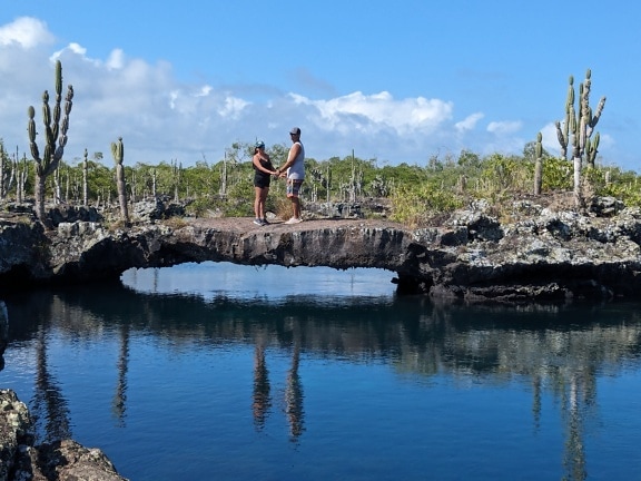 A man and a woman hold hands standing on a stone bridge over water on Isabela Island in natural park in Galapagos