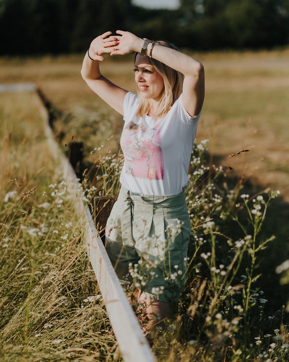 Χαρούμενη αγρότισσα στέκεται σε έναν εξοχικό κήπο με τα χέρια ψηλά