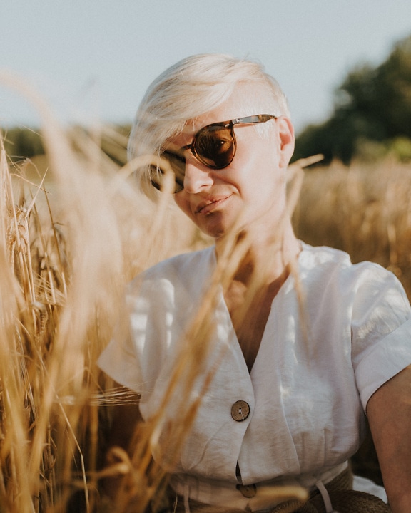 Portrait of a pretty young woman with short hair in a field of wheat at bright sunny summer day