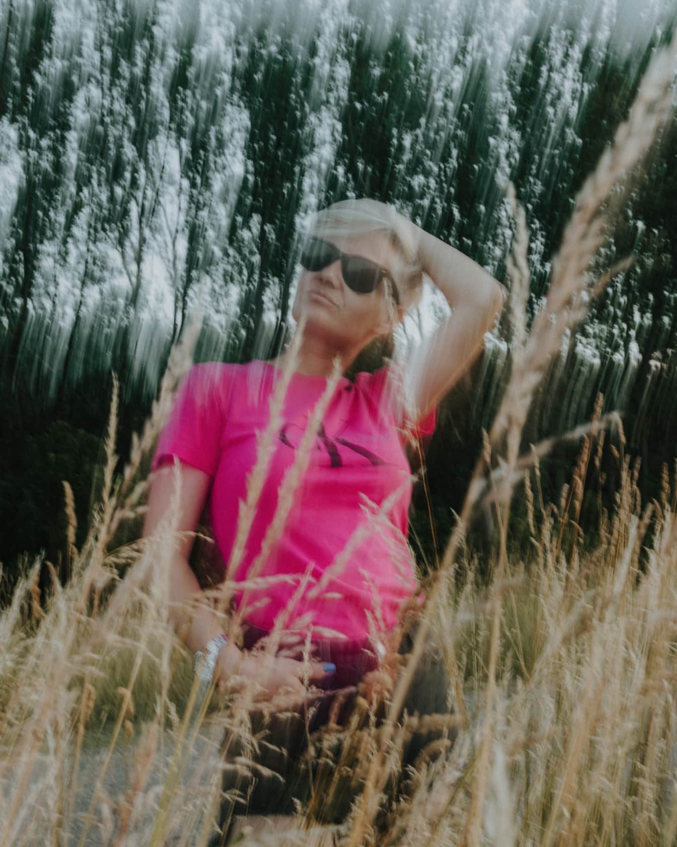 Porträtt av en kvinna i en rosa skjorta i ett fält av högt gräs med avsiktlig konstnärlig oskärpa