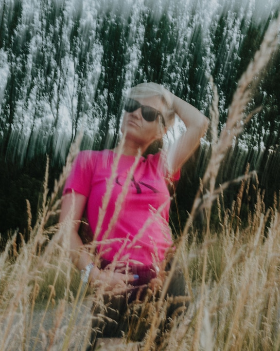 Ritratto di una donna in una camicia rosa in un campo di erba alta con sfocatura artistica intenzionale