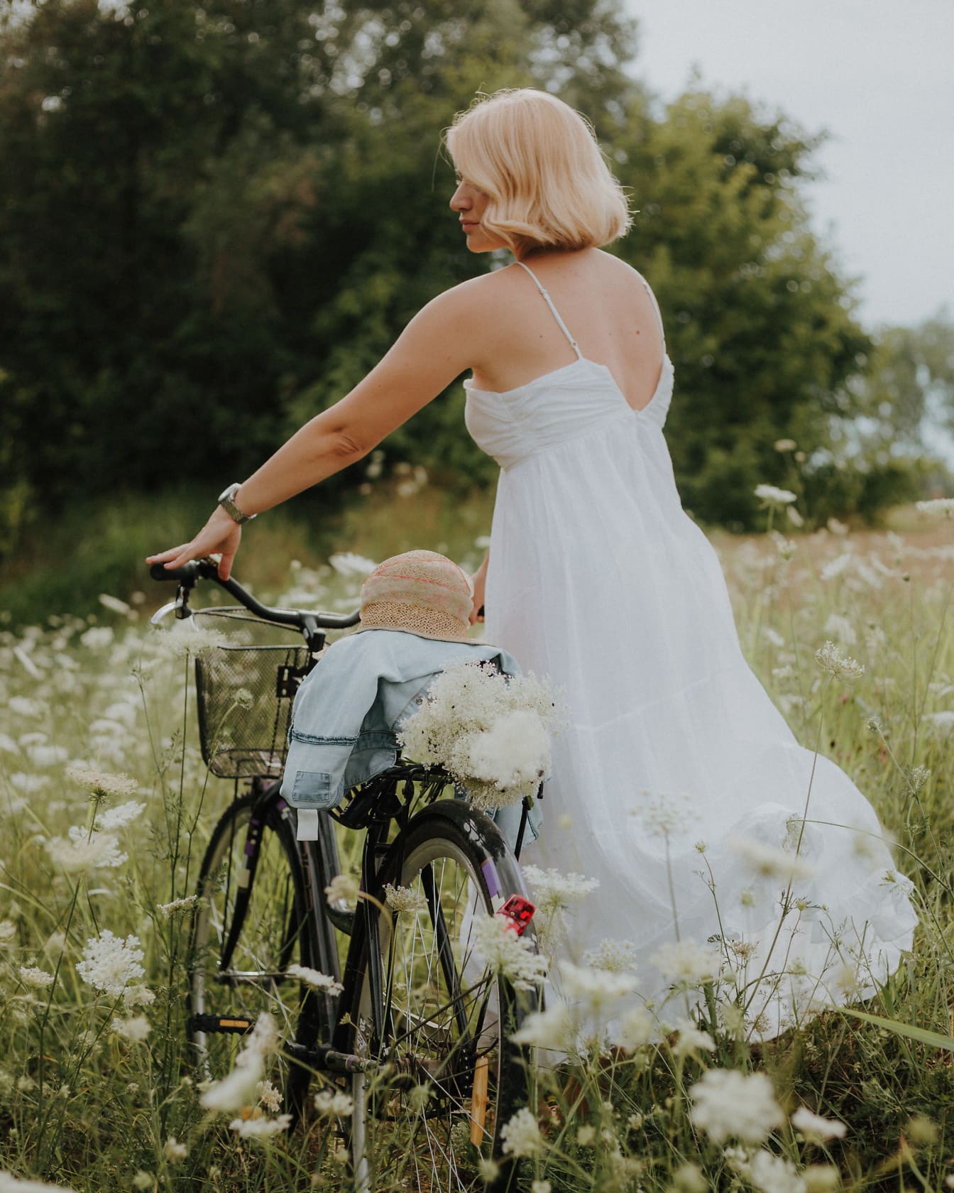 Người phụ nữ nông thôn tóc vàng đẹp trai trong một chiếc váy trắng với một chiếc xe đạp trên cánh đồng hoa