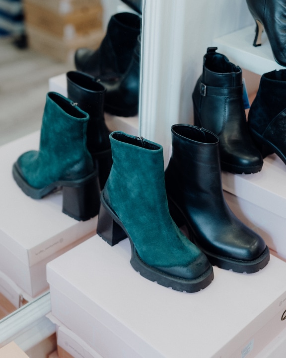 Fashionable dark greenish and black leather boots on a shelf next to a mirror in a footwear shop