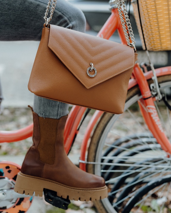 Close-up of a person’s leg sitting on a bicycle wearing brown boots and a holding a brown purse