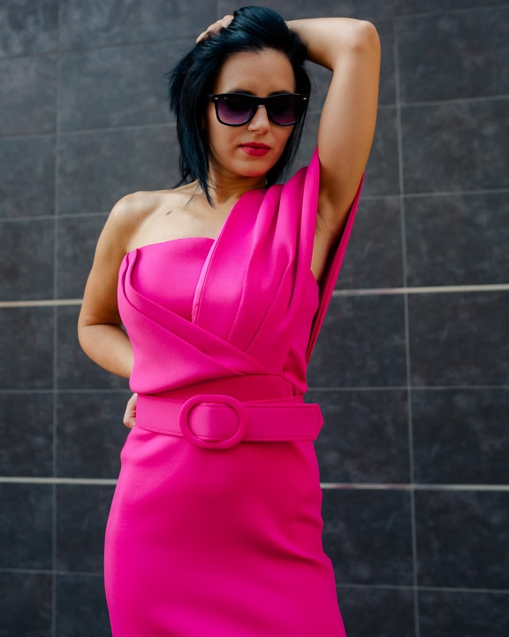 Stunningly beautiful businesswoman seductively poses with her hand in her hair in a fashionable new pink dress