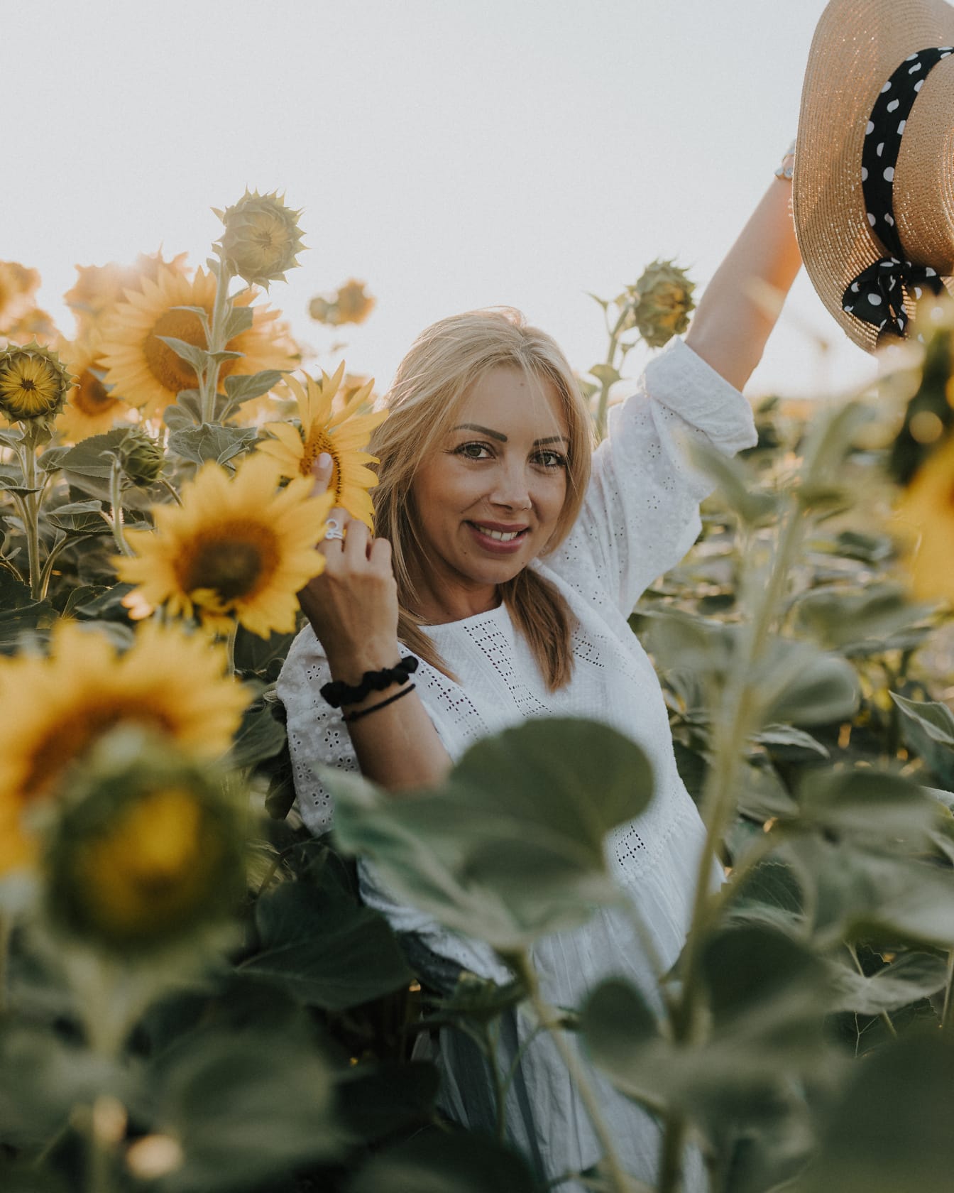 Portret van een glimlachende verbluffend mooie veedrijfster die een strohoed in een gebied van zonnebloemen houdt
