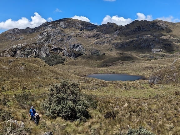 Zwei Wanderer wandern in einem grasbewachsenen Hügel mit einem See im Hintergrund im Naturpark Cajes in Ecuador