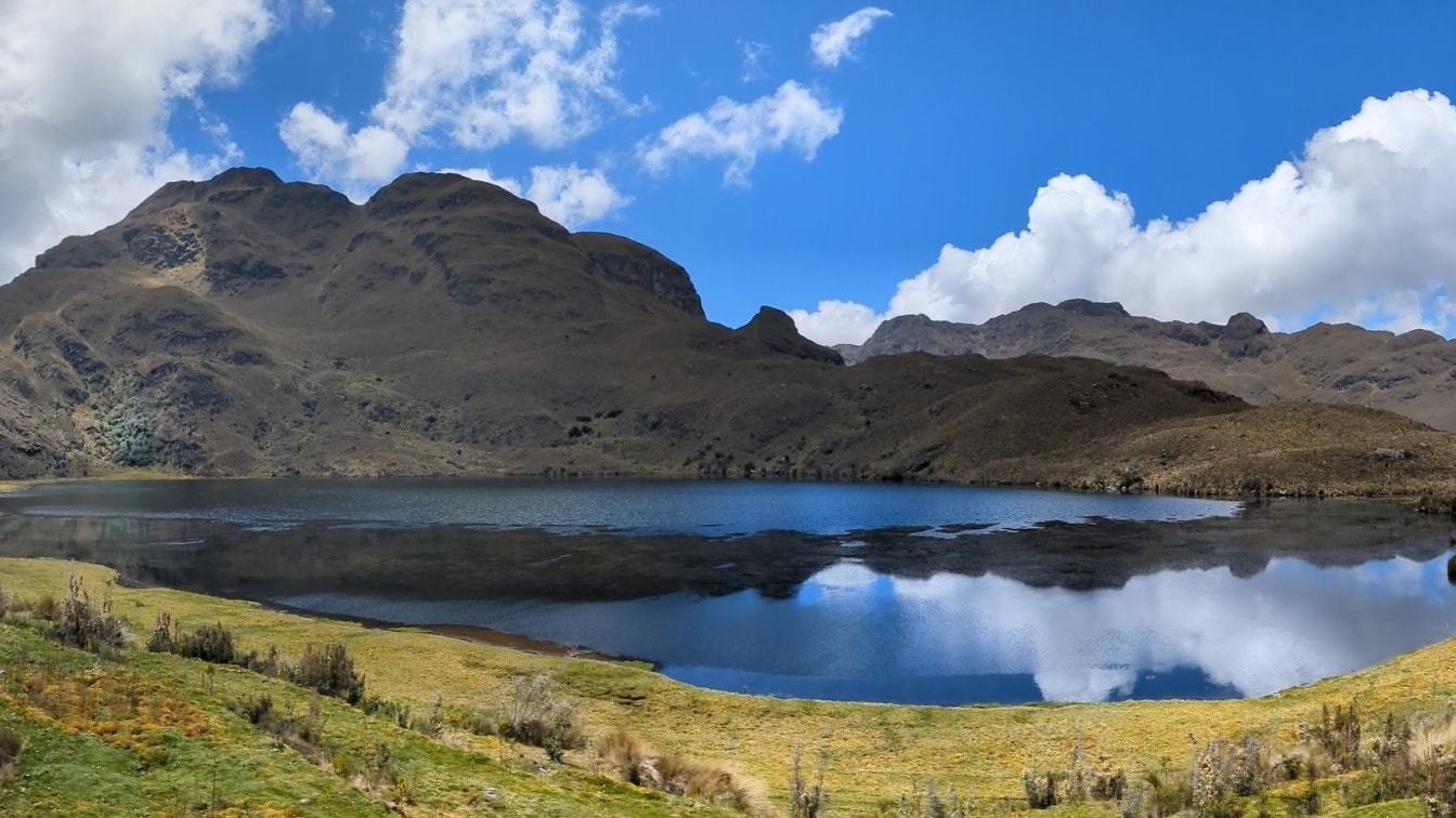 Landskap av naturparken Cajas i Cuenca kantonen med sjön Toreadora och med blå himmel med moln som reflekteras på lugnt vatten
