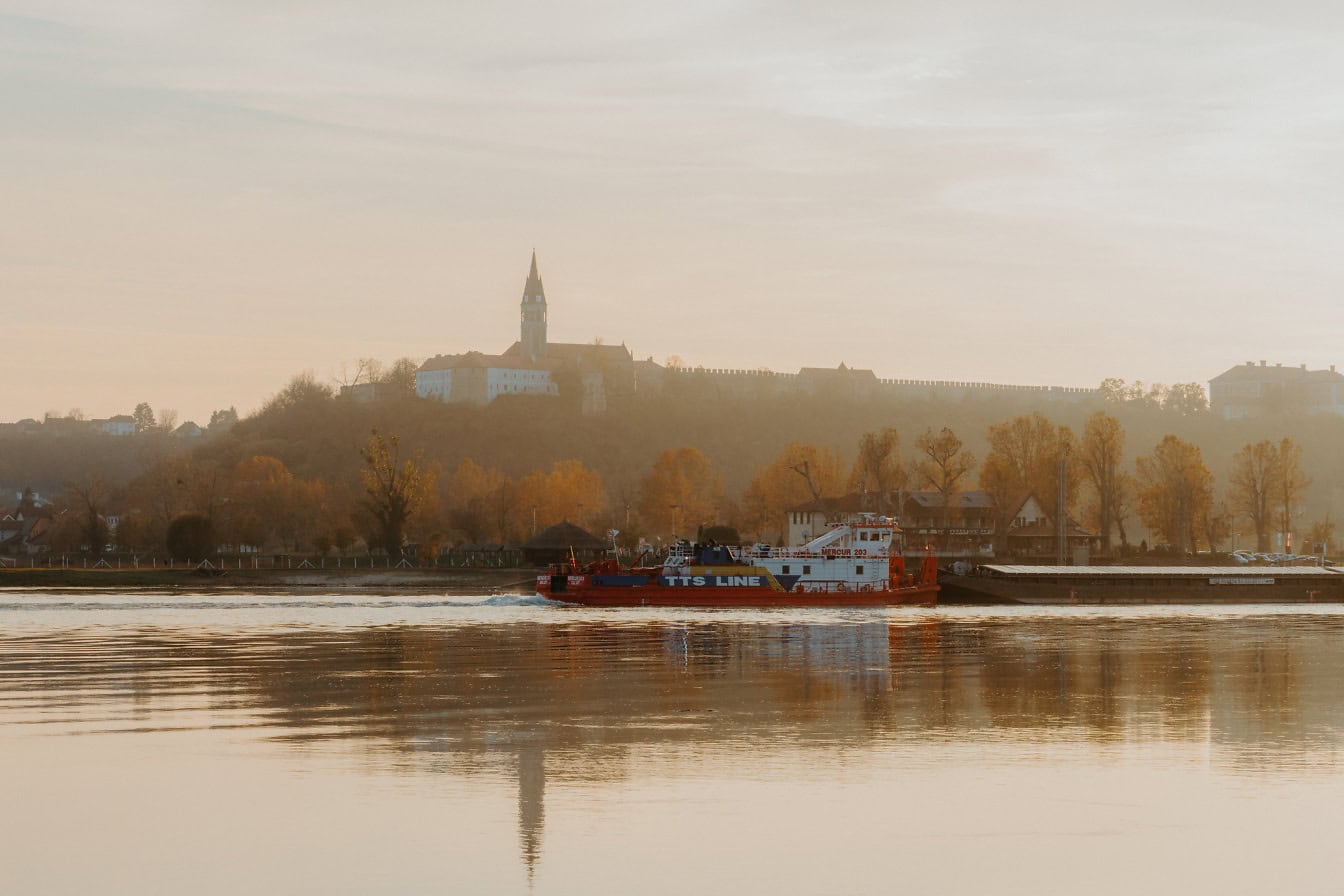Schiff auf der Donau mit Silhouette der katholischen Kirche des Heiligen Johannes Capistrano auf dem Hügel im Hintergrund in Ilok in Kroatien
