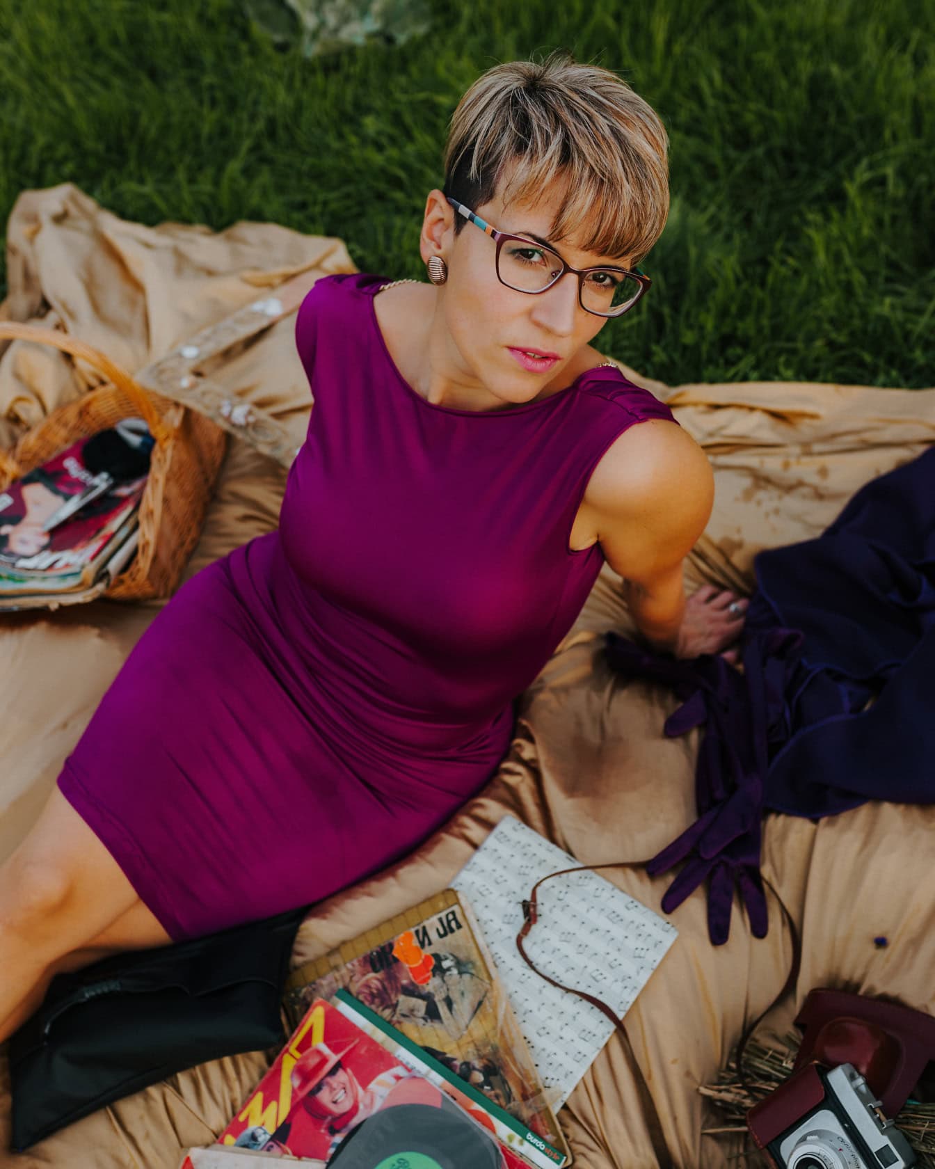 Femeie frumoasă cu coafură blondă scurtă în rochie violet stă pe o pătură de picnic