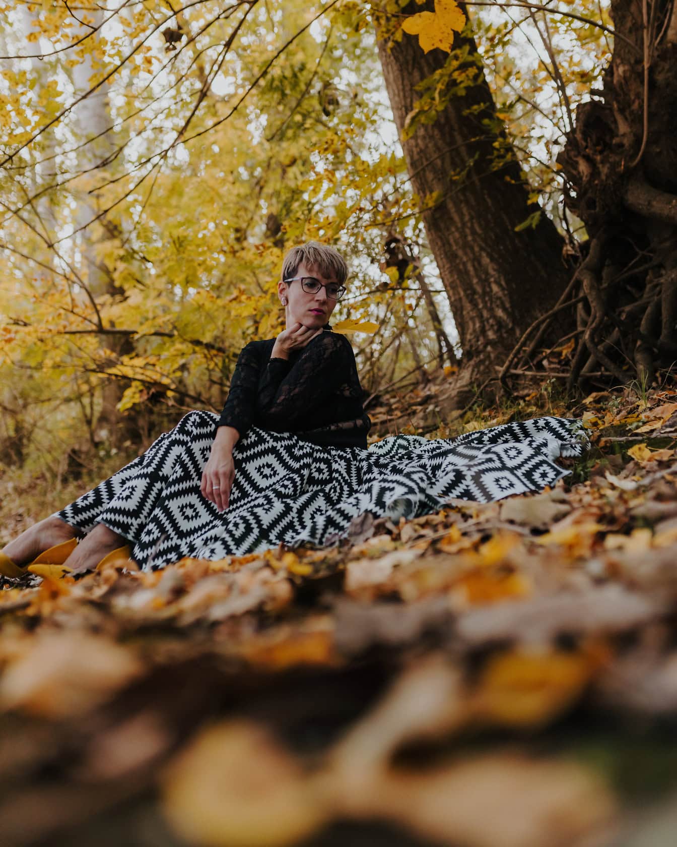 가을에 숲에서 나무 아래 흑백 치마에 앉아있는 여자