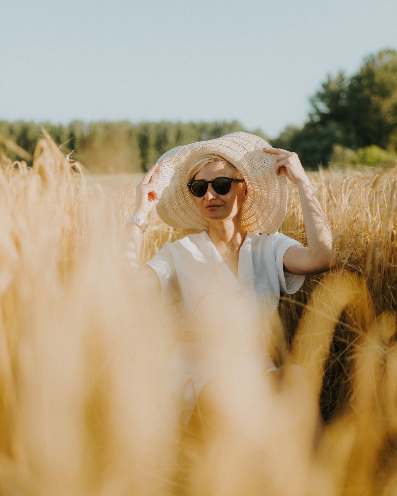 Kvinna som bär en hatt och solglasögon i ett fält av vete på varm solig sommardag