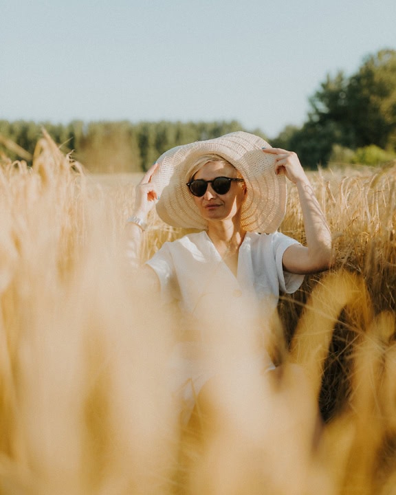 Woman wearing a hat and sunglasses in a field of wheat at hot sunny summer day
