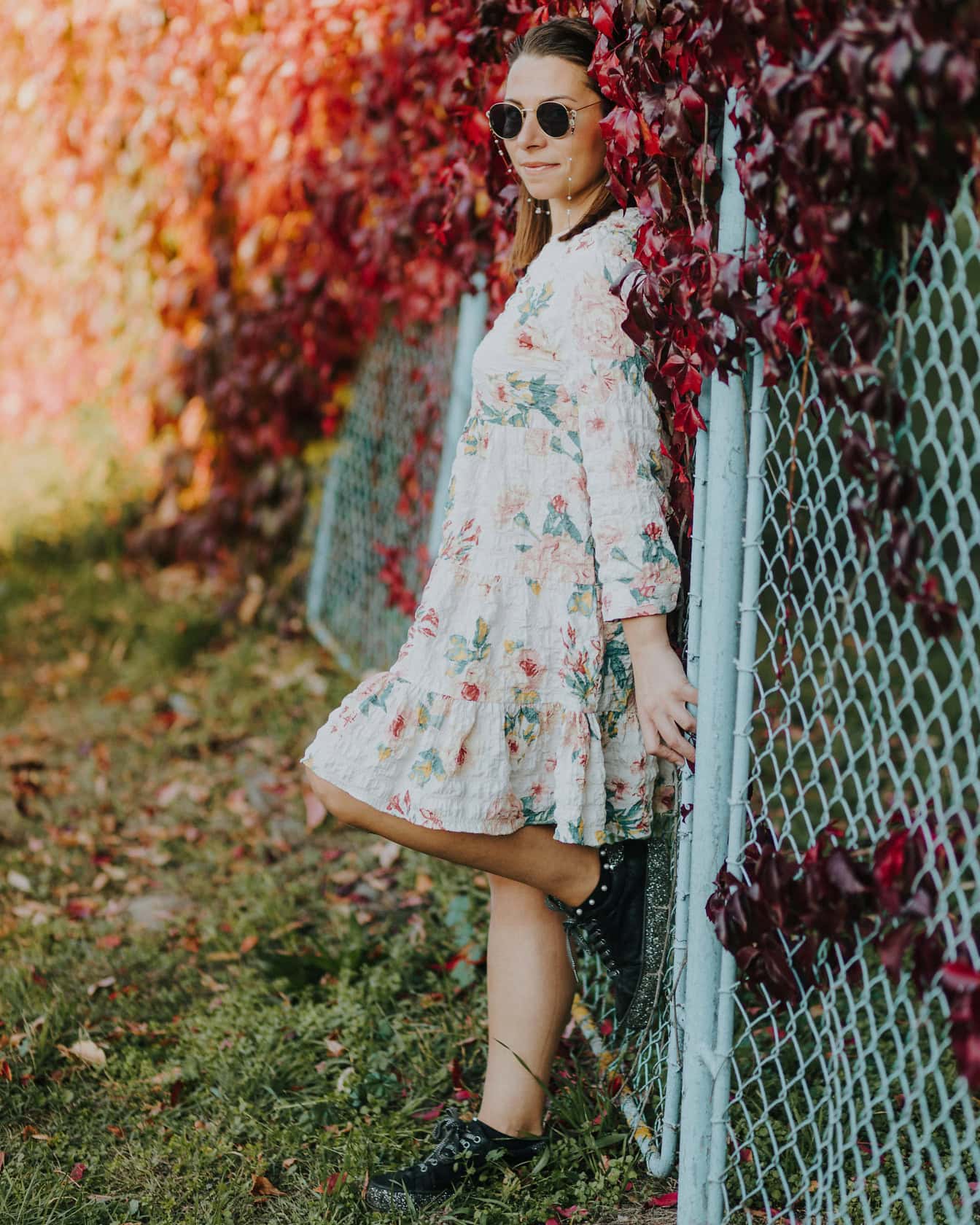 Fiatal, jóképű nő fehér virágmintás ruhában, a kerítésnek támaszkodva